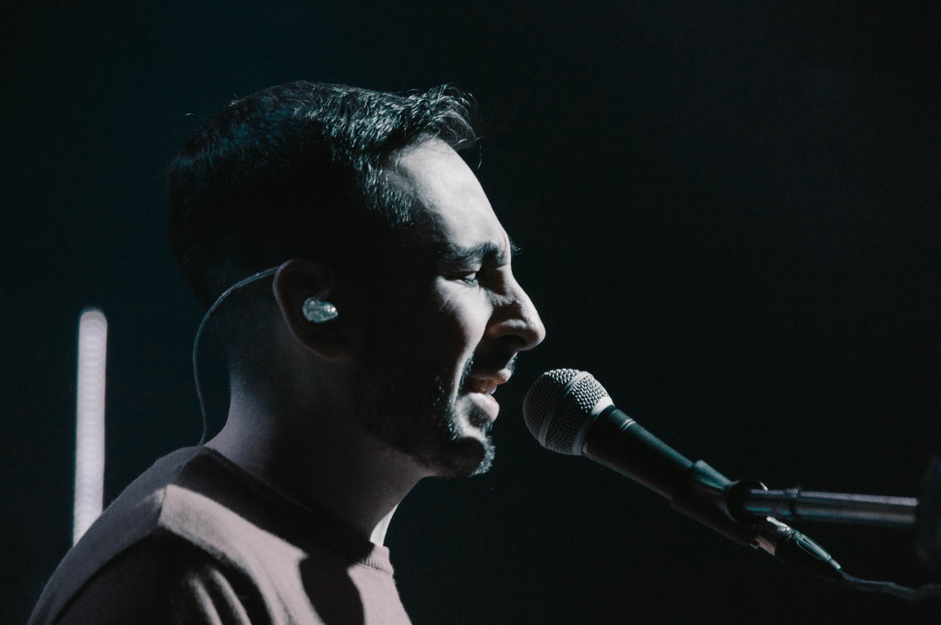 A singer at the microphone with an in-ear monitor and its cable visible